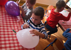 dzieci przy stolikach malują pisakami balony